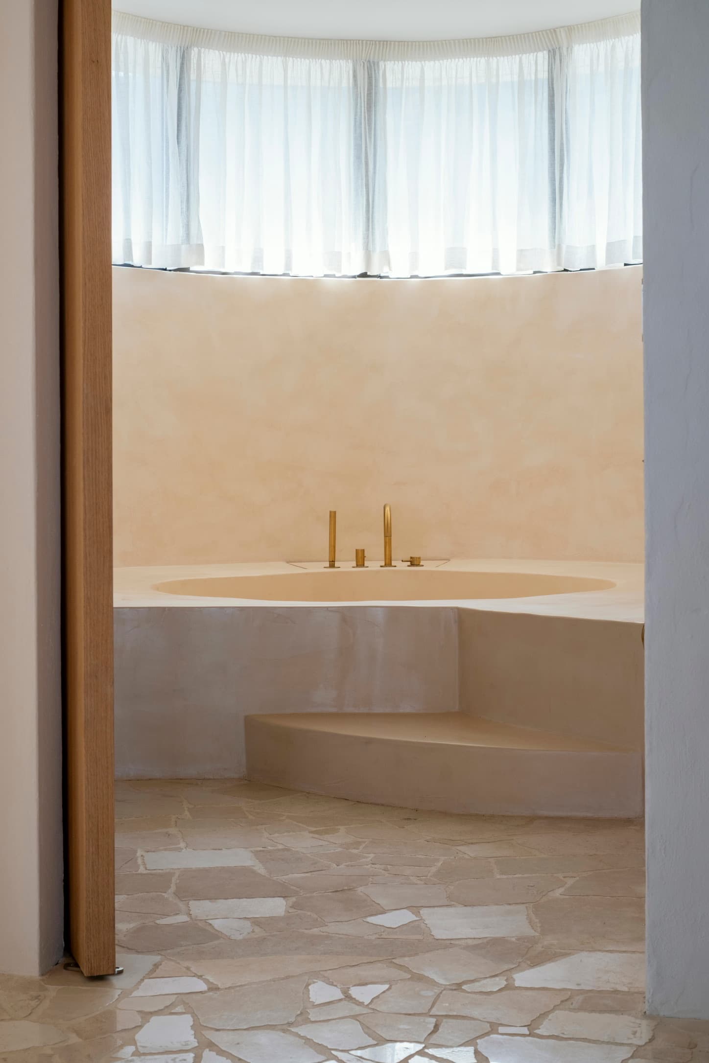 A round, sunken bath in smooth lime plaster with brass taps.