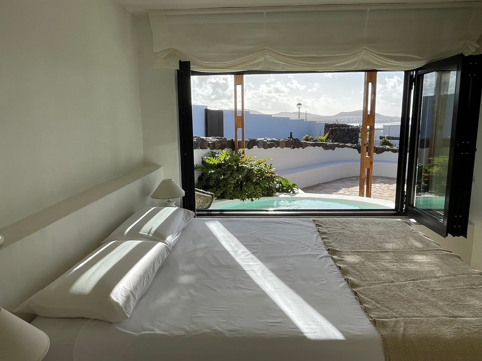 A bed beside open black-framed doors that lead to the terrace and the sea.