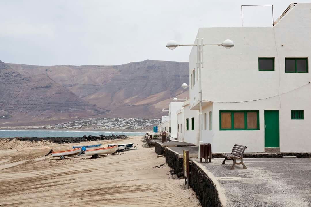 The suite behind a curved basalt wall on black volcanic ground below the Famara massif.