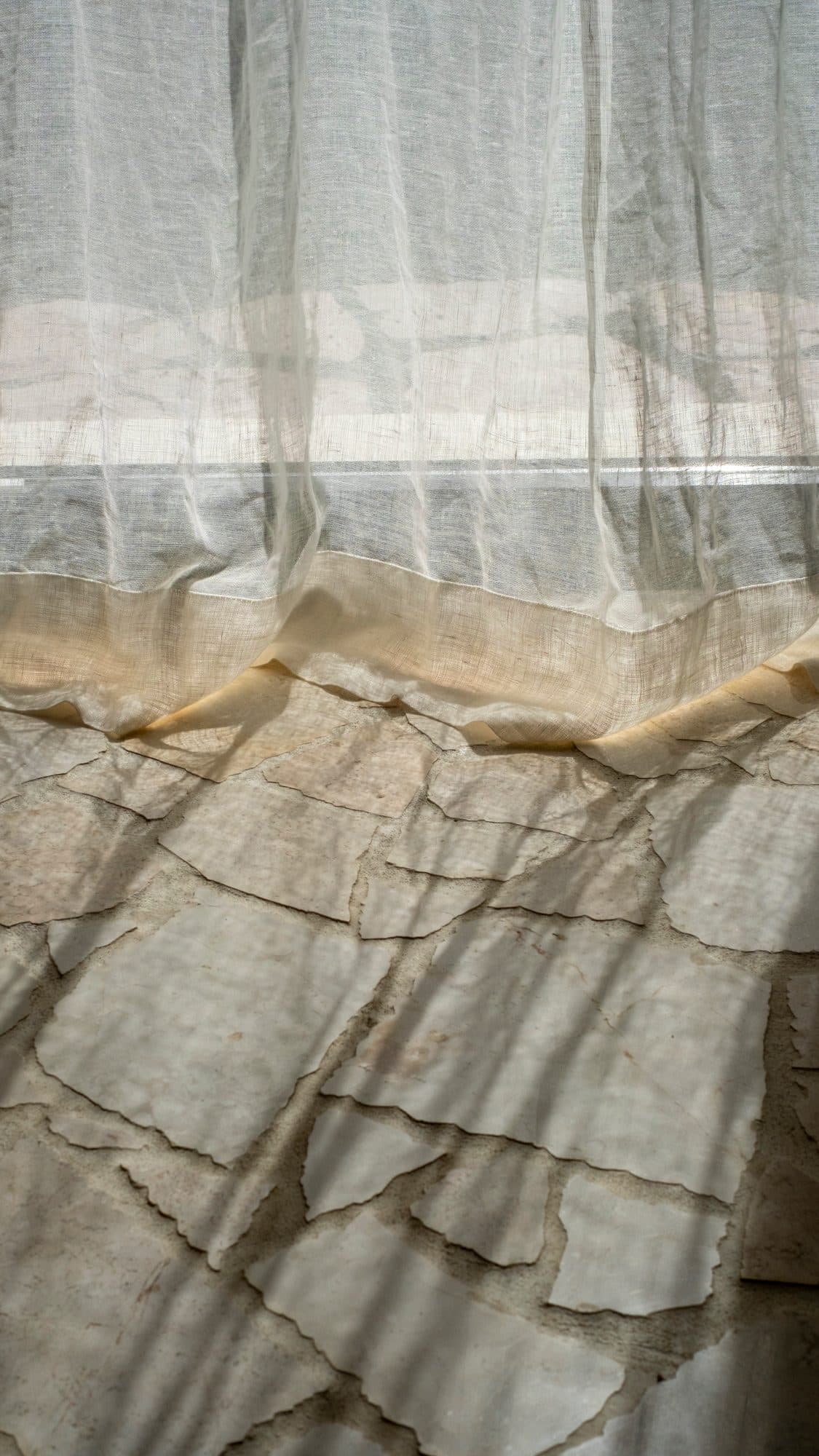 Linen curtain light falling across a floor of cracked pale stone.